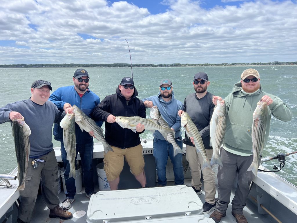 A group on a bachelor party holding striped bass. Fishing out of Boston.